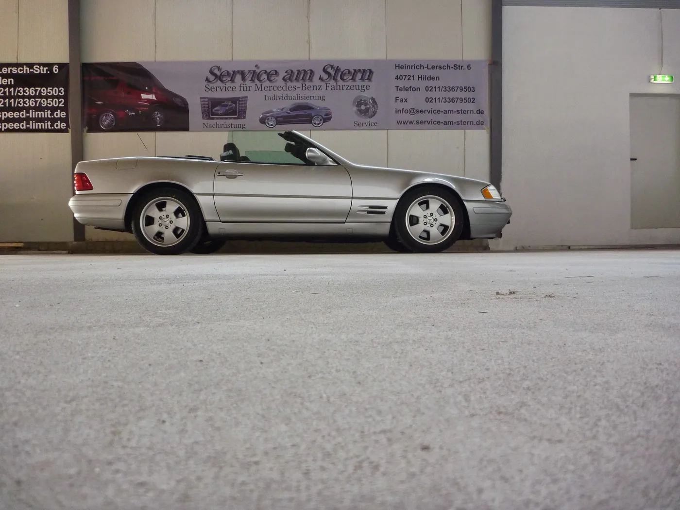 Silbernes Mercedes-Benz Fahrzeug als Roadster vor dem Service-am-Stern-Banner